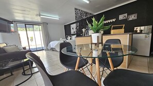 Un salon moderne avec une table à manger en verre, des chaises noires, un canapé et une grande plante en pot.