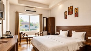 Habitación de hotel con cama, escritorio, sillas, aire acondicionado y ventana con cortinas.