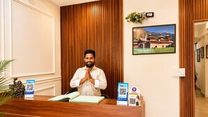 Un mostrador de recepción con un hombre detrás, un cuadro en la pared y un código QR para Paytm sobre el mostrador.