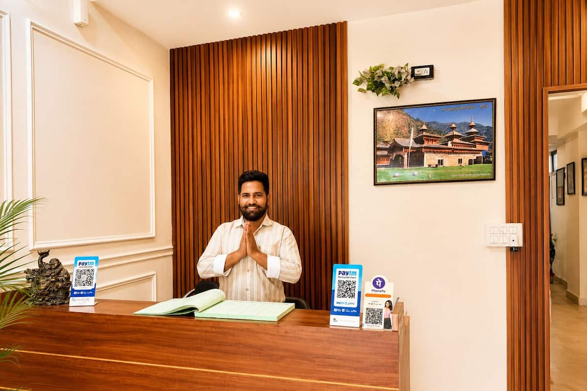 A reception desk with a man standing behind it, a framed picture on the wall, and a QR code for Paytm on the desk.