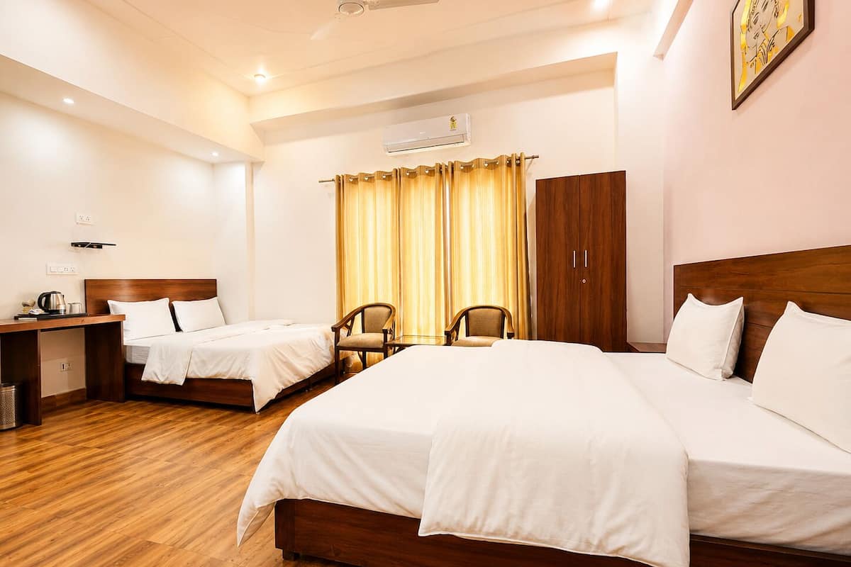 A hotel room with two beds, a wooden wardrobe, a desk with a chair, and an air conditioning unit.