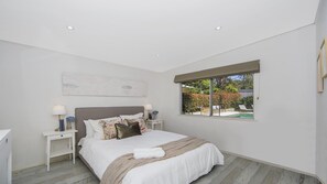 A bedroom with a bed, nightstands, a window with a view of a garden, and a ceiling with recessed lighting. - Stay 3 nights, pay 2 this Winter* (PEARL BEACH)