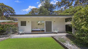 A small, single-story building with a covered patio, a bed, and two chairs. - Stay 3 nights, pay 2 this Winter* (PEARL BEACH)
