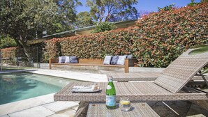 A poolside area with a wicker lounge chair, a wooden bench, and a bottle of alcohol. - Pet friendly,pool + stroll to beach and cafe (PEARL BEACH)