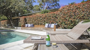 A poolside area with a wicker lounge chair, a wooden bench, and a bottle of alcohol. - Stay 3 nights, pay 2 this Winter* (PEARL BEACH)