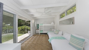 Una habitación con literas, ventilador de techo, ventana grande y vistas al exterior con vegetación.