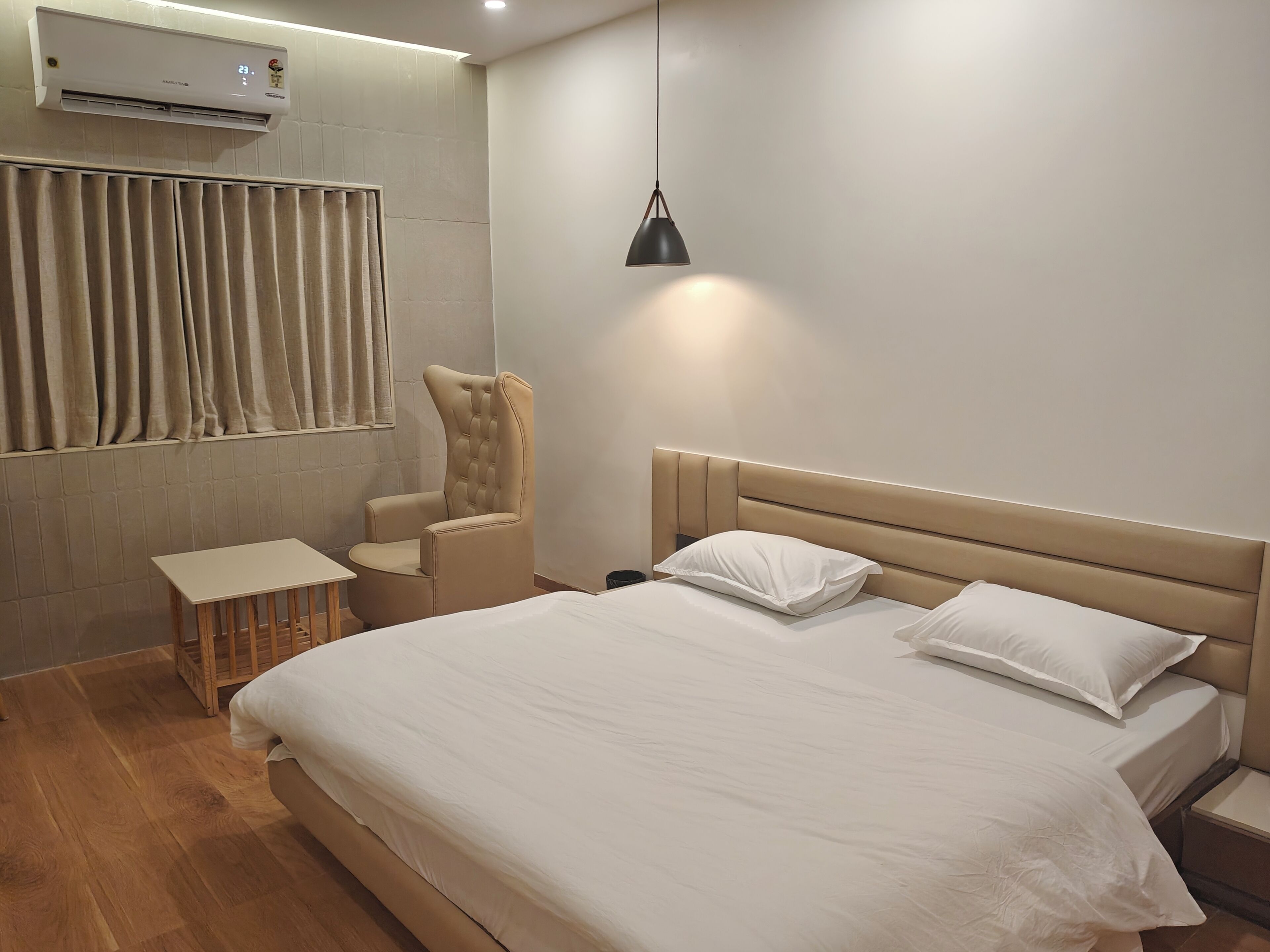 Un dormitorio con cama, una silla, una mesita de noche, una lámpara y un equipo de aire acondicionado.