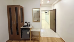 A hallway with a wooden floor, a kitchenette area with a coffee maker, a small refrigerator, and a cabinet with glass doors.