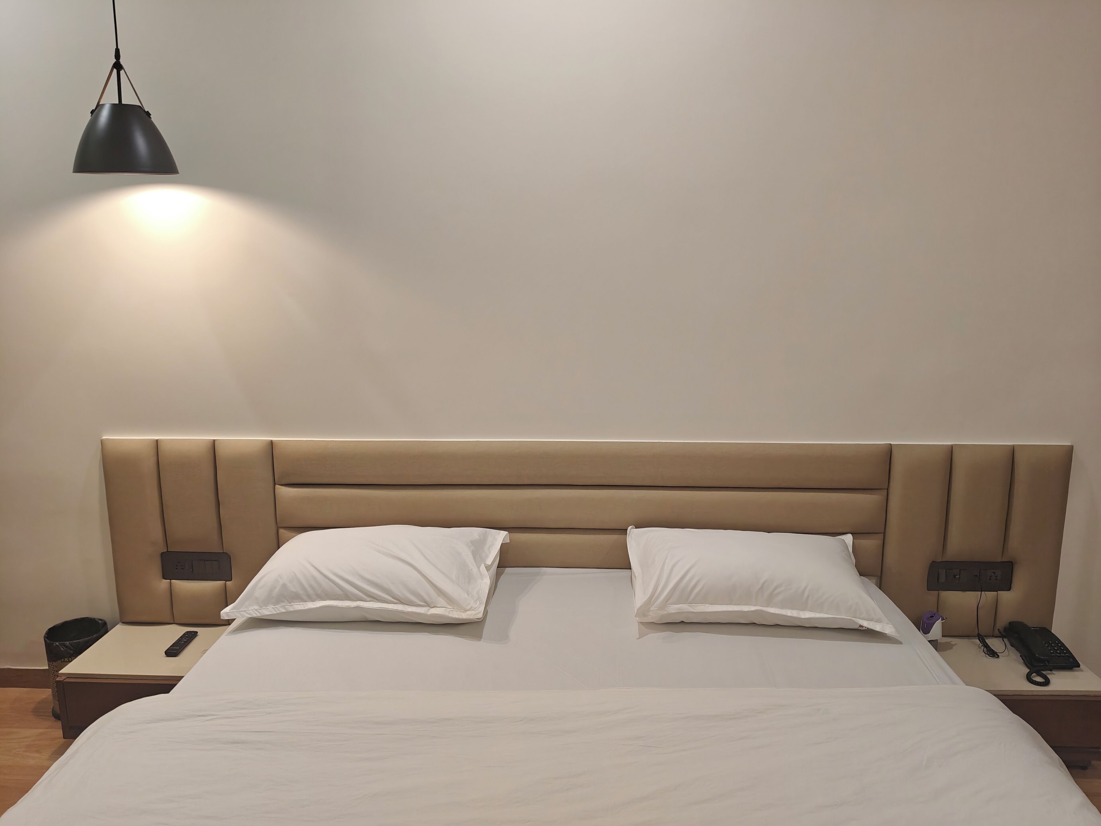 A hotel room with a large bed, two bedside tables, a bedside lamp, and a power outlet on the headboard.