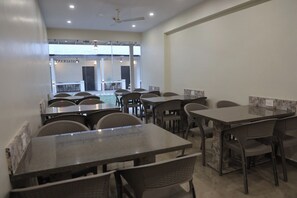 A modern dining area with multiple tables and chairs, a ceiling fan, and a view of the outdoor area. - HOTEL KRISHIV (Sanand)