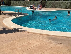 Ein Schwimmbecken mit einer gefliesten Terrasse, einer Metallleiter und einigen Personen im Wasser.