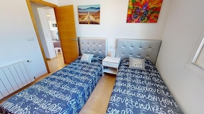 A room with two beds, a nightstand, a door, and a wall with a painting. - Villa - Stay6 - Garden - Parking - Pool - Golfarea (Torre-Pacheco)