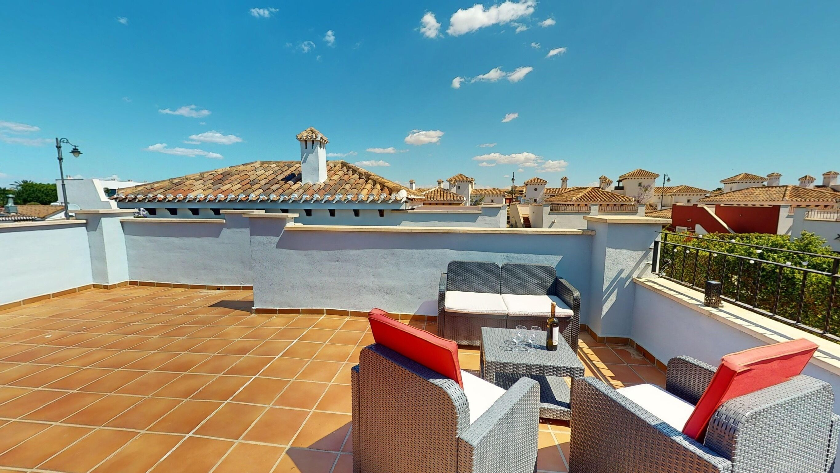 A rooftop terrace with tiled flooring, wicker furniture, and a clear view of surrounding buildings.