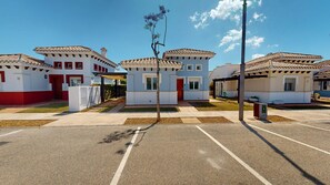 A row of white buildings with red accents, a parking lot, and a clear sky. - Villa - Stay6 - Garden - Parking - Pool - Golfarea (Torre-Pacheco)