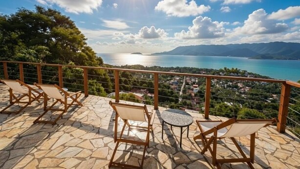 Una terraza con suelo de piedra, sillas de madera y una mesa con vistas a un paisaje costero que incluye montañas y una masa de agua.