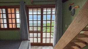 Una habitación con una cama, un ventanal con vistas, una escalera de madera y un mural de tucán en la pared.