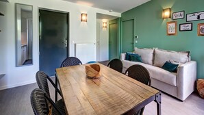 Une pièce comprenant une table à manger en bois, des chaises en osier, un canapé blanc et des lampes fixées au mur.