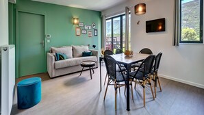Un salon moderne avec un mur d’accent vert, un canapé, une table à manger avec des chaises, un téléviseur et une grande fenêtre offrant une belle vue.