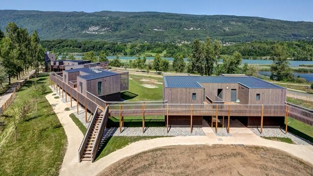 Un bâtiment moderne doté d’un toit plat, d’un espace extérieur couvert et offrant une vue sur un lac et des collines.
