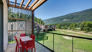 Un balcon doté d’une terrasse en bois et de chaises rouges, offrant une vue sur une pelouse verdoyante et un paysage montagneux.
