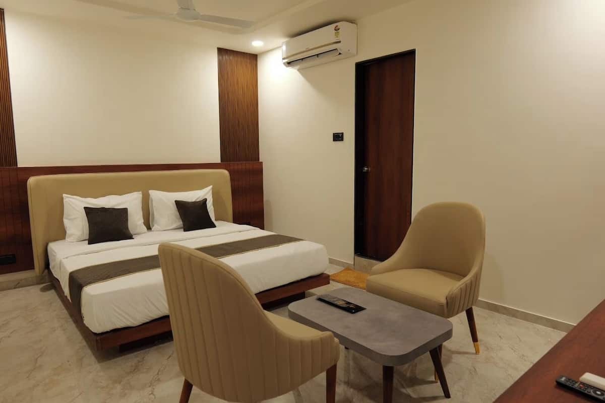 A hotel room with a bed, two chairs, a small table, an air conditioning unit, and a door.