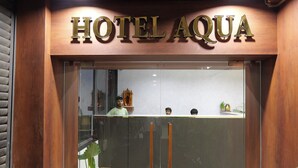 Balcão de recepção de hotel com uma placa indicando 'HOTEL AQUA' e uma planta em vaso à esquerda.