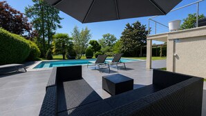 Ein Poolbereich mit überdachter Sitzecke und umliegendem Grün.
