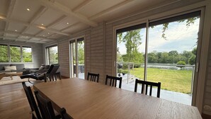 Ein geräumiger Essbereich mit einem langen Tisch und Stühlen, großen Fenstern mit Seeblick und viel Grün, sowie eine gemütliche Sitzecke mit Sofa und Sesseln.