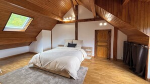Ein Schlafzimmer mit schrägen Wänden, einem Oberlicht, einem Bett, einer Tür und einer Gardinenstange.
