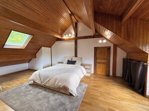 Une chambre avec un plafond en pente, un puits de lumière, un lit, une porte et une tringle à rideaux.