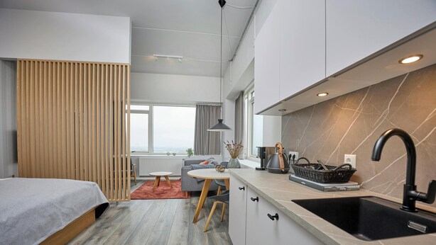 Eine moderne Küche mit Spüle, ein Essbereich mit Tisch und Stühlen sowie ein Bett mit Holz Kopfteil.