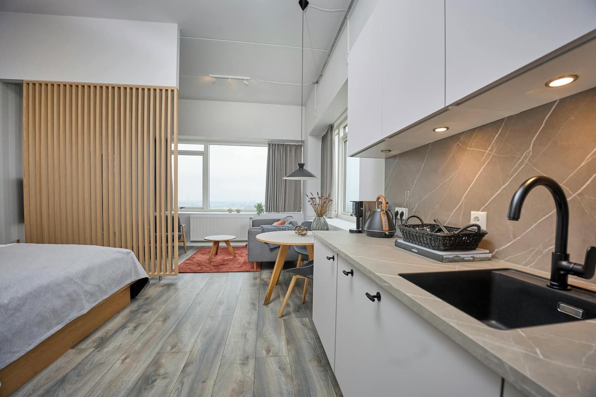 Una cocina moderna con un lavamanos, una zona de comedor con una mesa y sillas, y una cama con cabecera de madera.