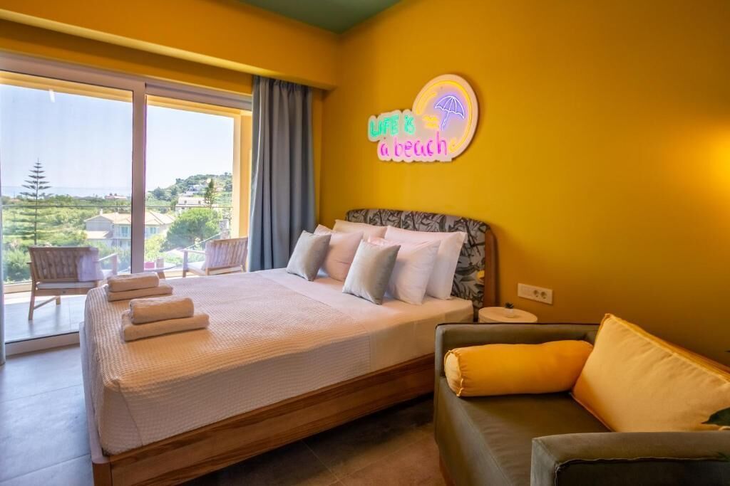A bedroom with a bed, a sofa, a neon sign, and a view of the outdoors.