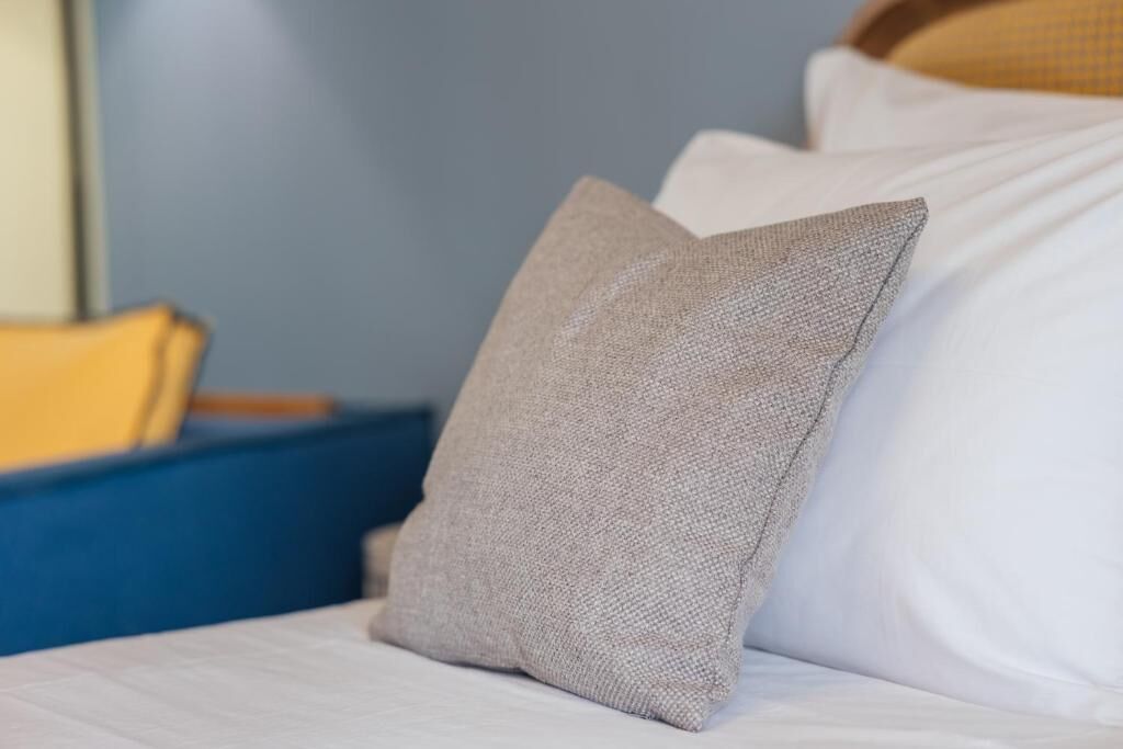 A bed with a white pillow and a textured pillow.
