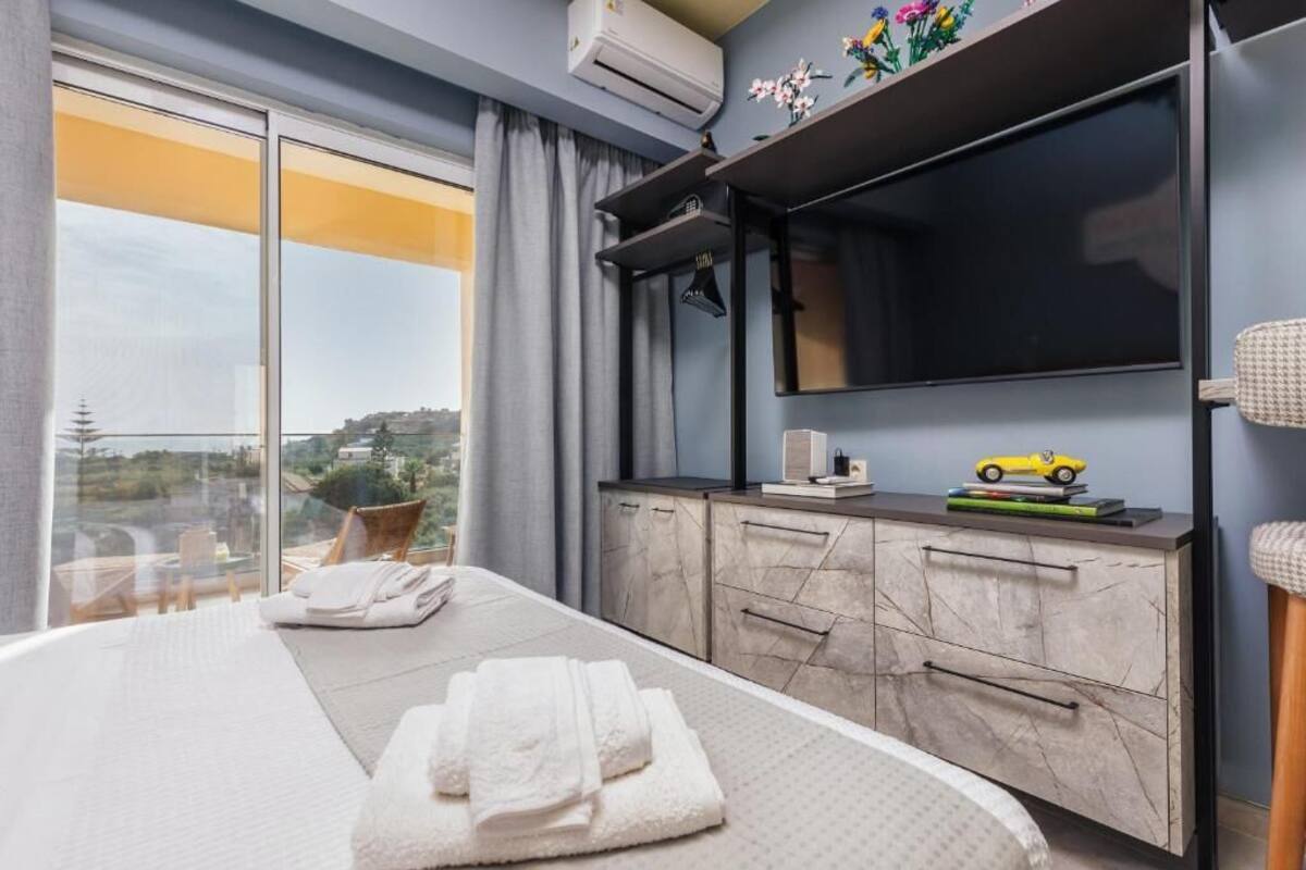 A hotel room with a bed, a TV, a minibar, and a view of the city.