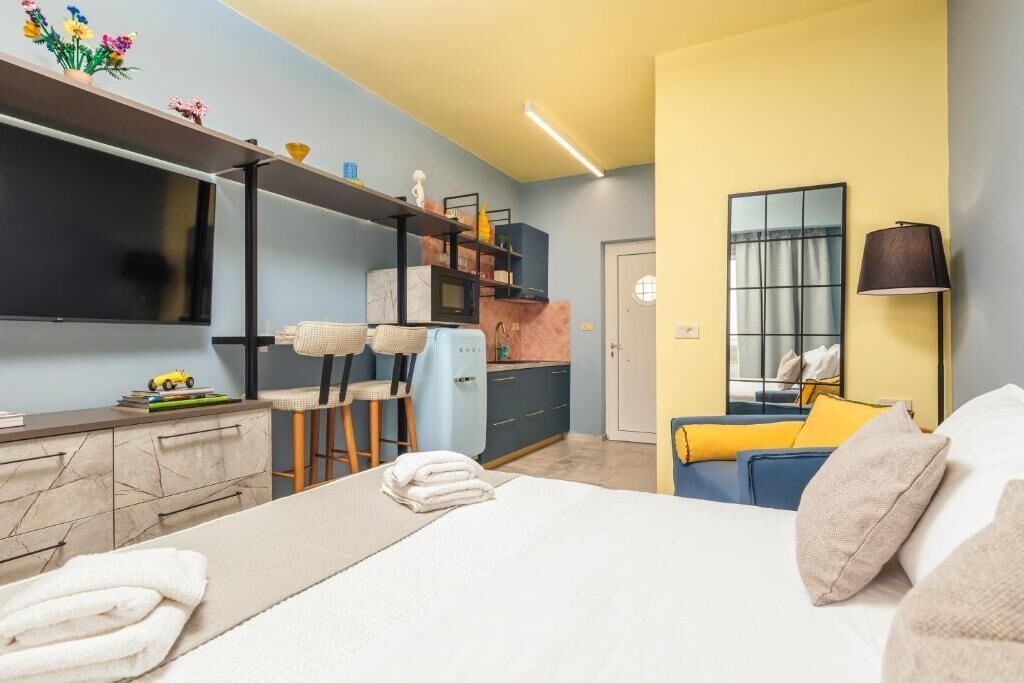 Een moderne hotelkamer met een bed, bureau, stoel, televisie, kitchenette en een badkamer.