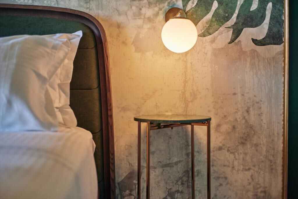 Een bed met wit beddengoed, een klein krukje en een wandlamp.