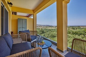 A balcony with wicker furniture, a glass table, and a view of a green landscape. - ap boutique apartments (Zakynthos)