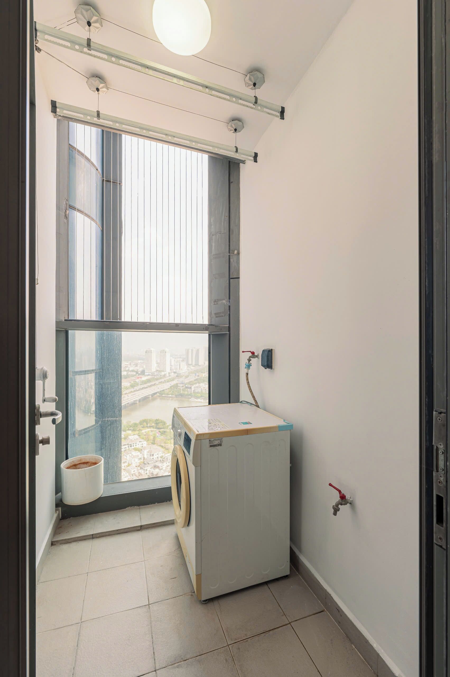 Une buanderie équipée d’un lave-linge, d’une fenêtre avec des stores, d’un radiateur et d’un robinet.