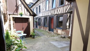 A narrow courtyard with a small table and chairs, potted plants, and a building with exposed timber framing.