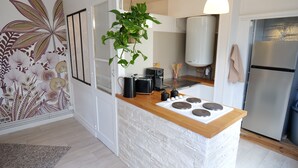 A modern kitchen with a central island, a hanging plant, a white water heater, and a stainless steel refrigerator.