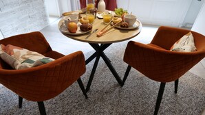 A breakfast table with a variety of food items and drinks, two orange chairs, and a white brick wall in the background.