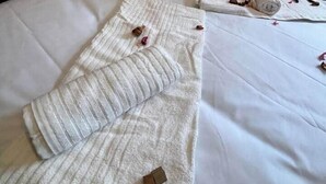 Ein ordentlich gemachtes Bett mit Kissen, einem gefalteten Handtuch und Rosenblättern auf einem Hotelbett.