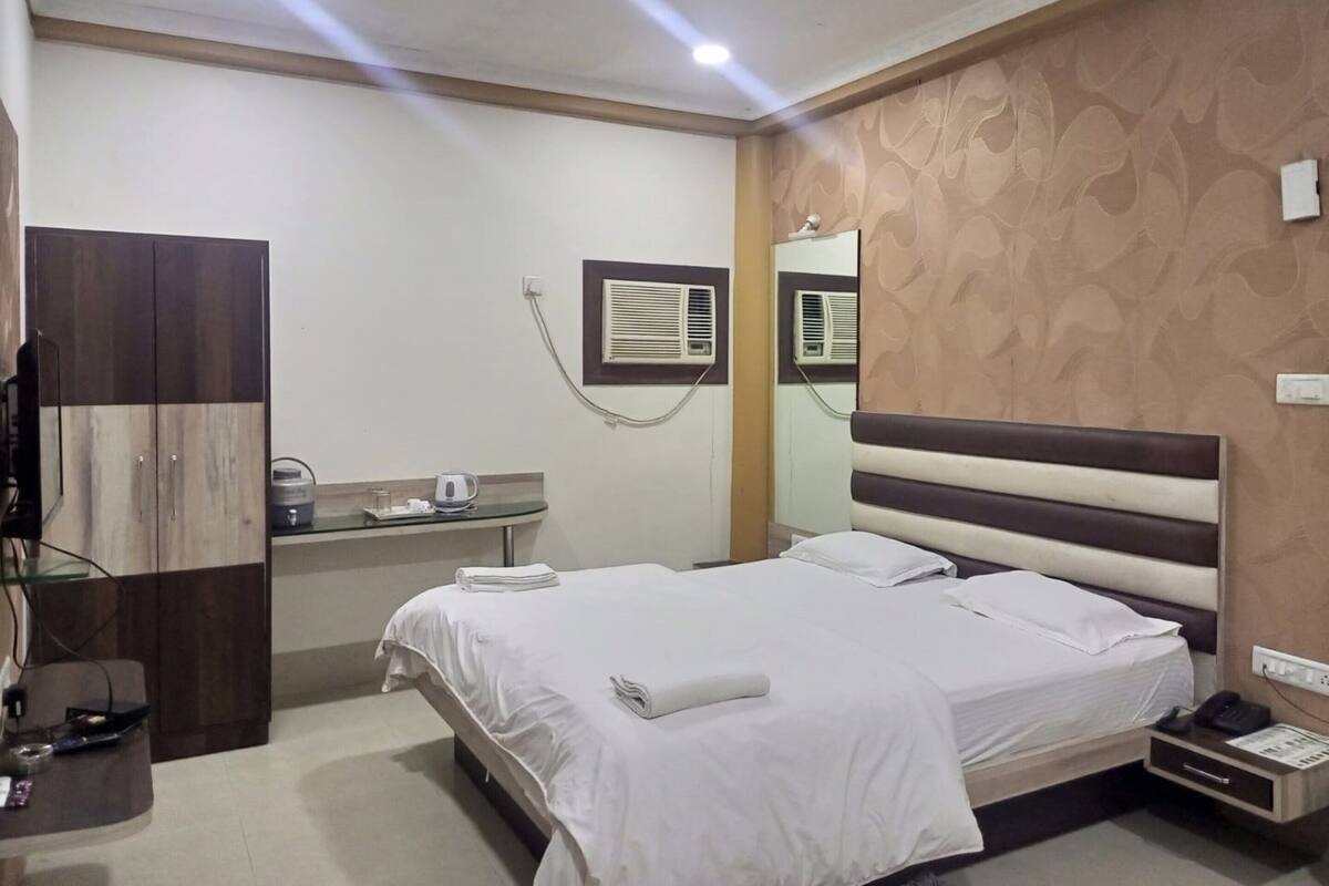 Habitación de hotel con cama, escritorio con silla, armario, ventilador de techo y aire acondicionado de pared.