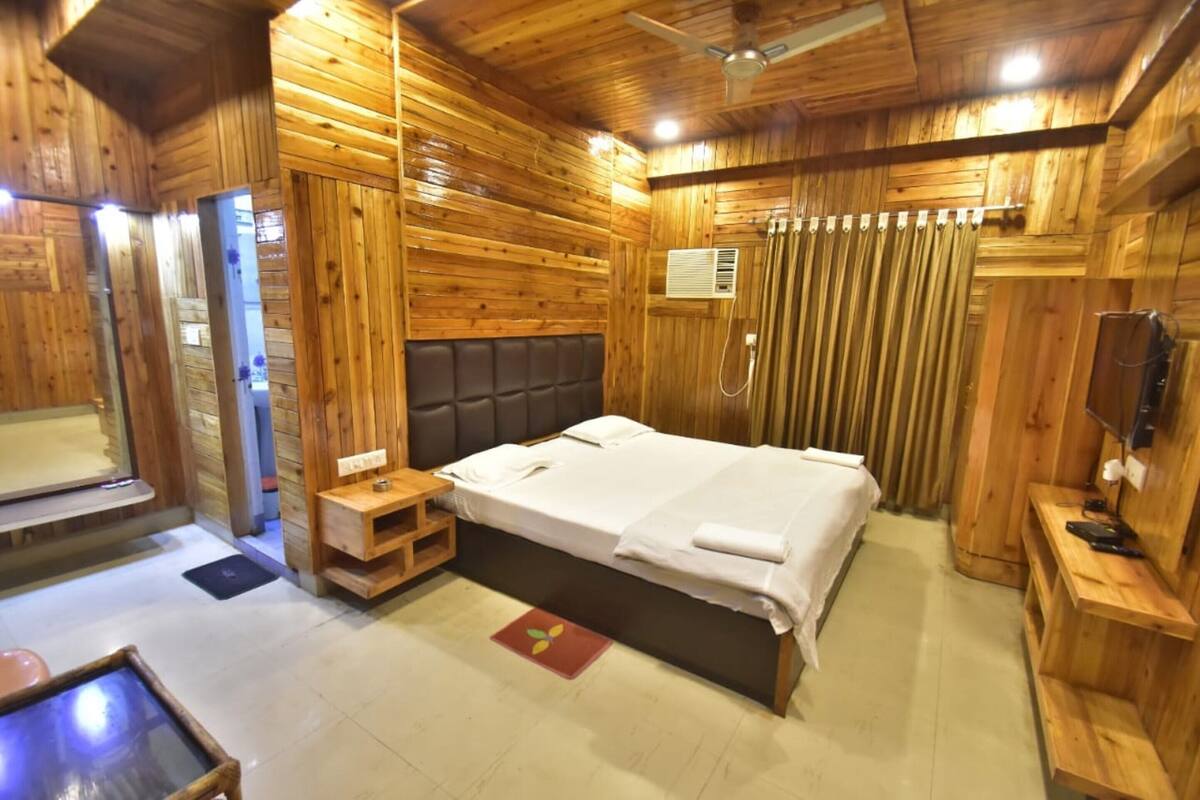 Una habitación tipo cabaña de madera con una cama, una mesita, un banco y un ventilador de techo.