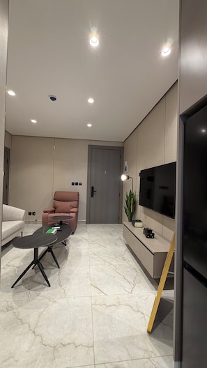 A modern living room with a sofa, a pink chair, a coffee table, a TV, and recessed ceiling lighting. - 201 Tara-jre Jabal Al Lweibdeh With Stunning View (Amman)