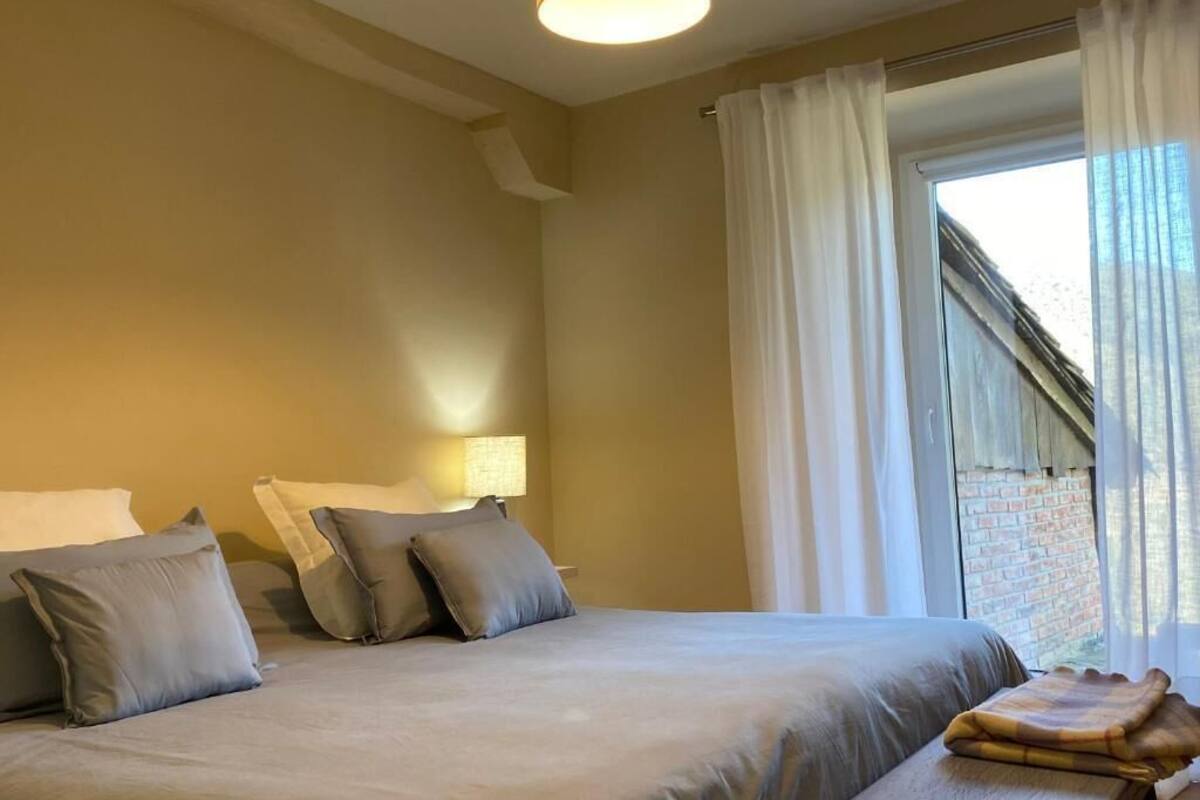 Une chambre à coucher avec un lit, des oreillers, une lampe, une fenêtre avec des rideaux et une vue sur un mur de briques.