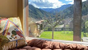 A window with a view of a mountainous landscape, a colorful pillow, and a brown cushioned seat. - apartamentos calm and nature (Cabezón de Liébana)