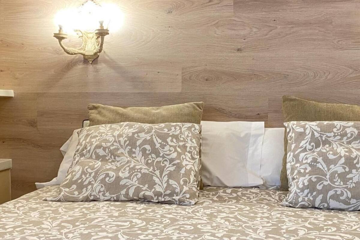Un lit avec une literie à motifs, un luminaire fixé au mur et une tête de lit en bois.