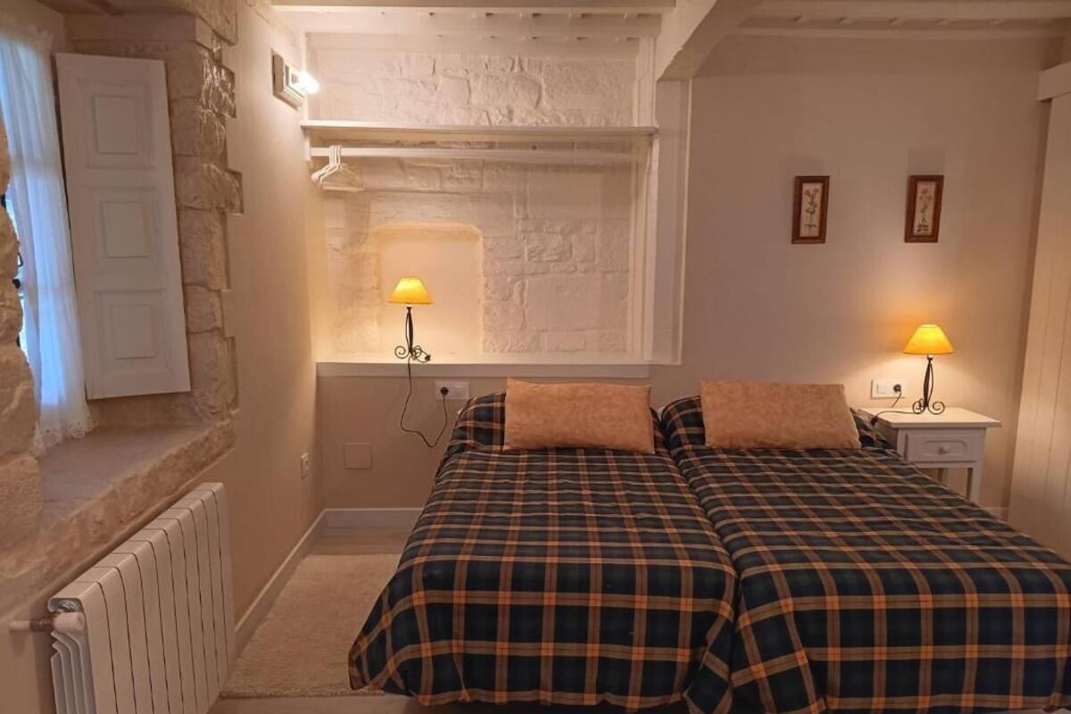 Une pièce chaleureuse avec deux lits, un mur en pierre, un radiateur blanc et deux lampes de chevet.